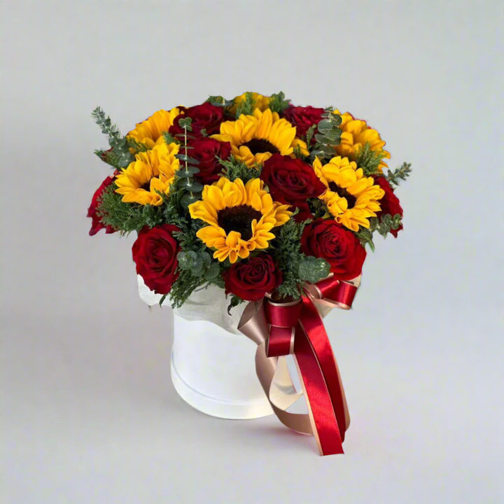 Bouquet with 8 sunflowers, 15 red roses, eucalyptus, and green fillers arranged in a round white box by florist dubai